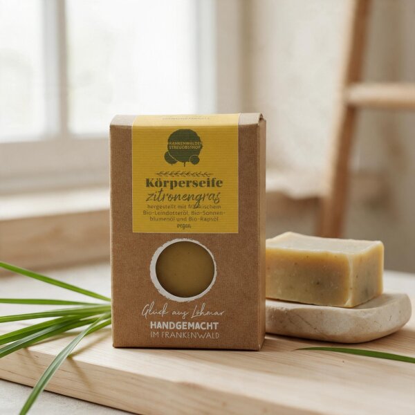 Vegane Körperseife Zitronengras vom Frankenwälder Streuobsthof in brauner Kartonverpackung neben Seifenstück und Zitronengras